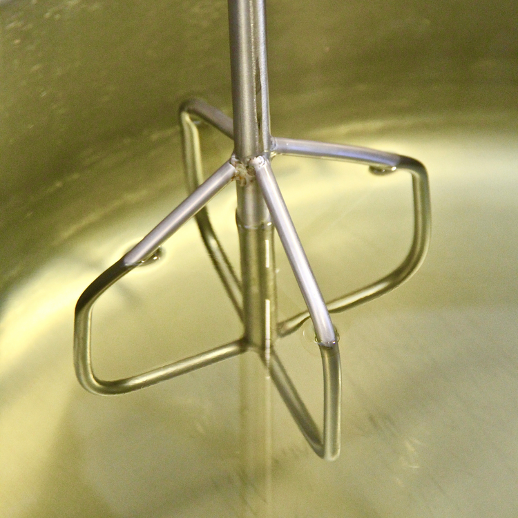 Metal mixer in vat of gold fragrance oil 