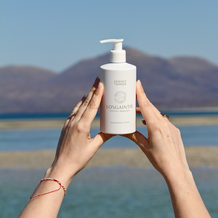 Losgaintir Hand & Body Lotion being held in two hands with Isle of Harris beach landscape in the background