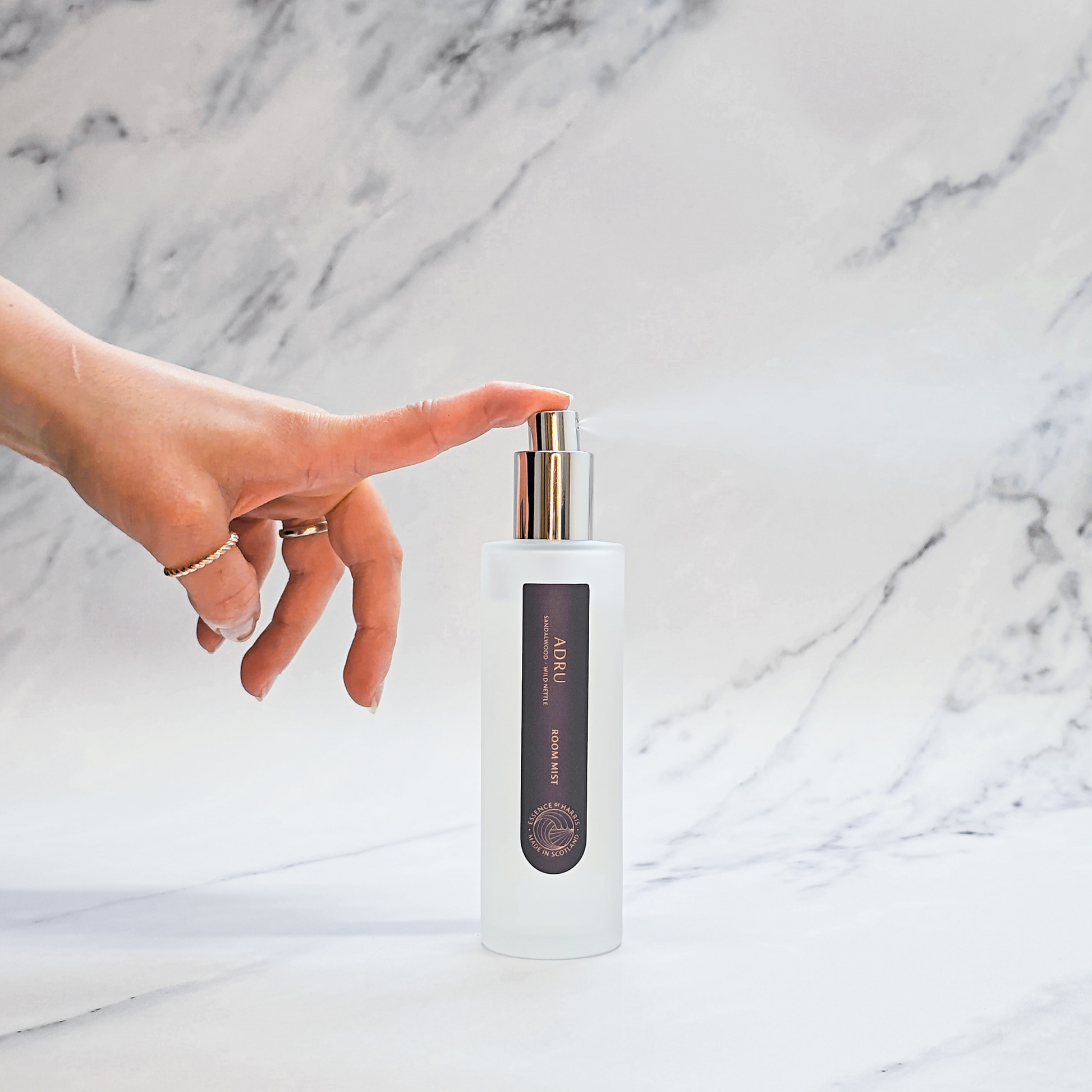 Essence of Harris Adru sandalwood and wild nettle room spray on marble backdrop with hand spritzing spray