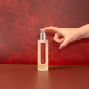 Frosted Cranberry Room Spray in frosted glass with silver spray cap photographed on a red festive background. With manicured hand pressing down on spray cap.