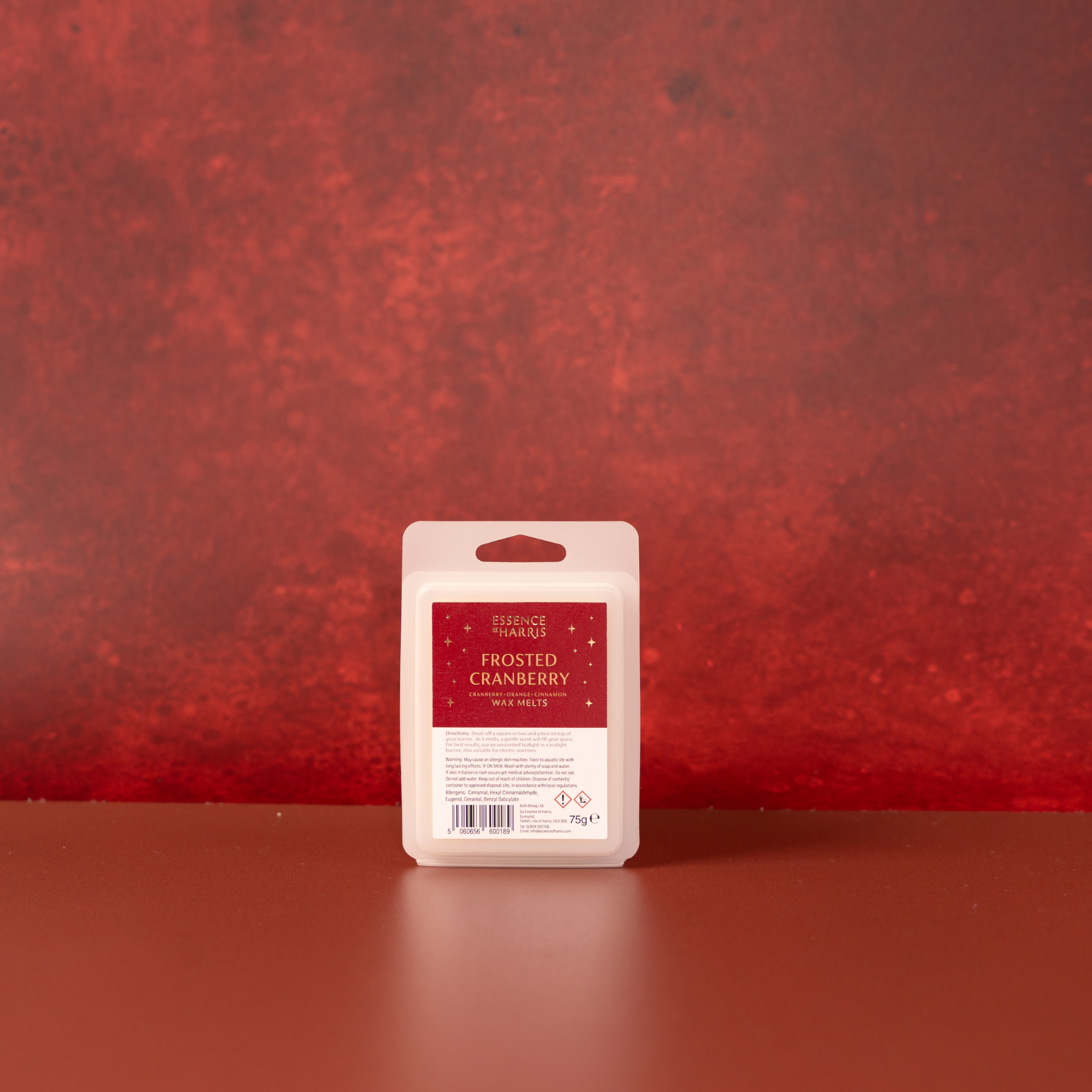 A single packaged wax melt bar labeled 'Frosted Cranberry' by Essence of Harris, standing upright on a matching red surface against a textured red background.