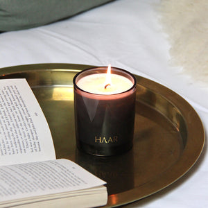 Haar, black glass fig scented candle on a gold tray next to open book.