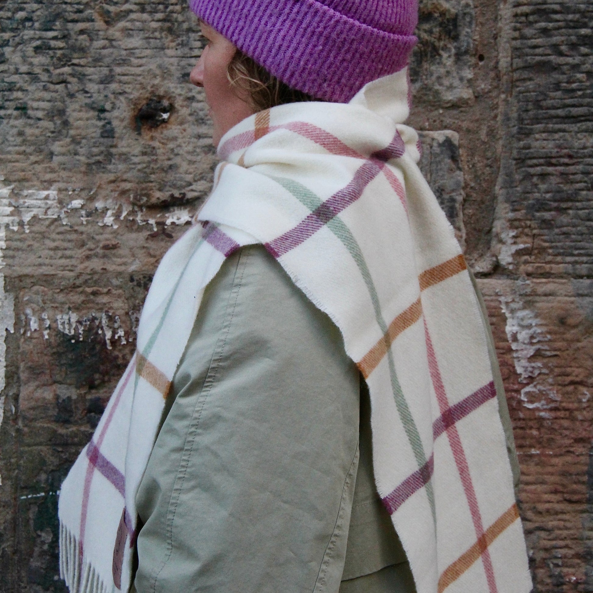Essence of Harris, Harris Sands pastel checked lambswool scarf worn by a woman with a green jacket and purple woolen hat