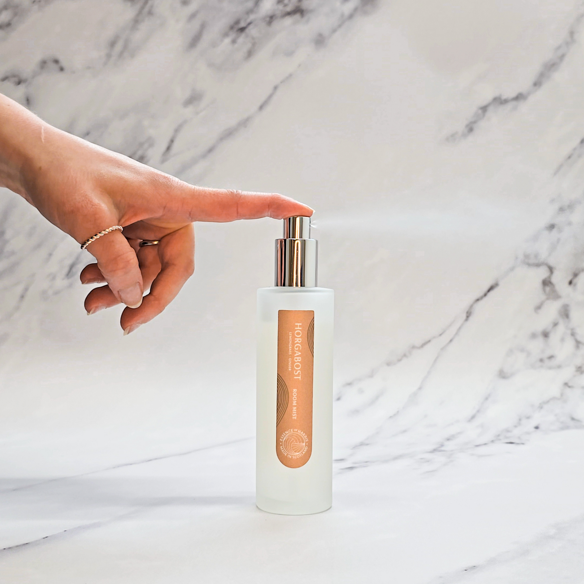 Essence of Harris Horgabost lemongrass and ginger room spray on marble backdrop with hand spritzing spray