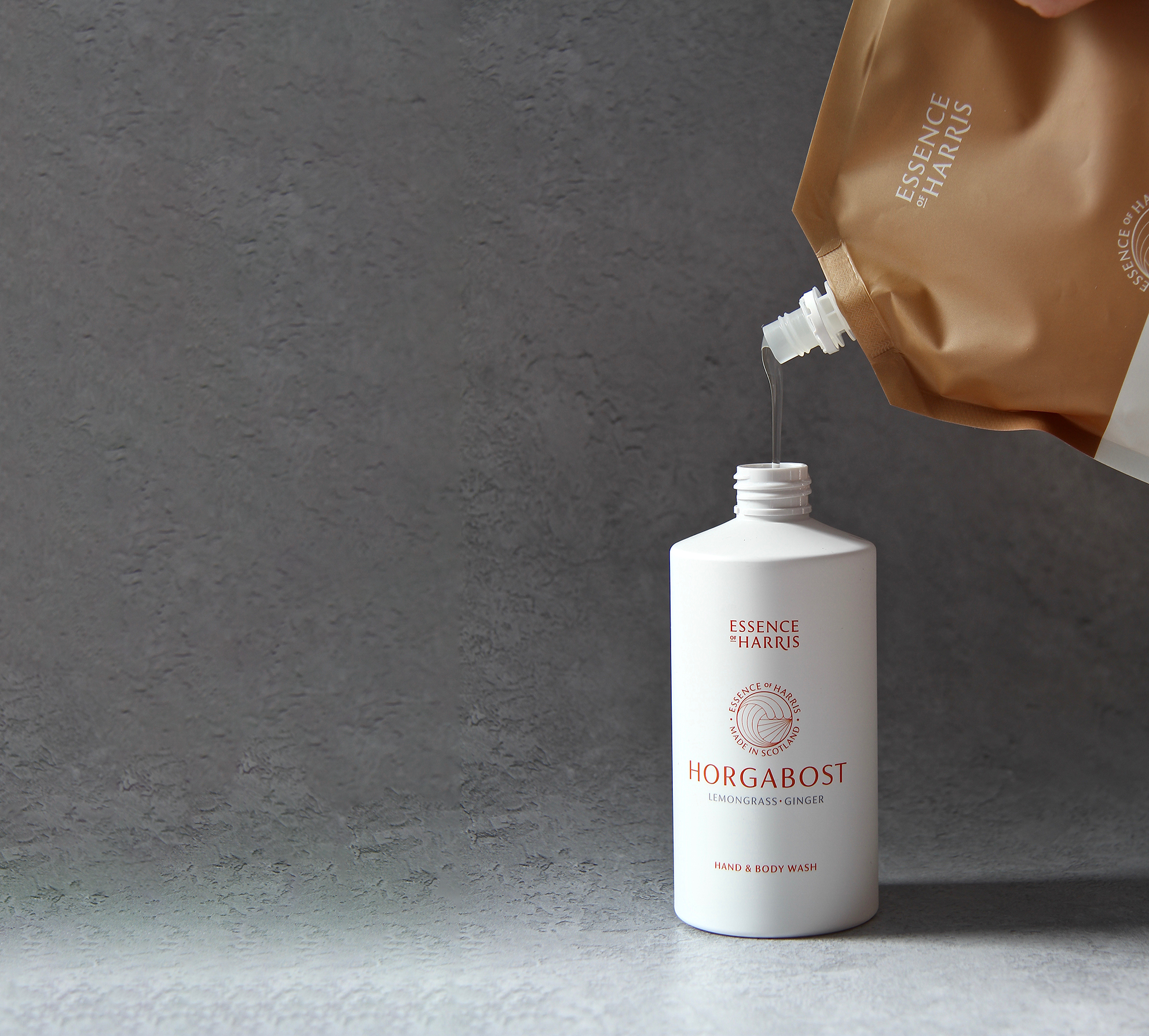 Horgabost, lemongrass and ginger hand and body wash being refilled with a pouch on a grey stone background.