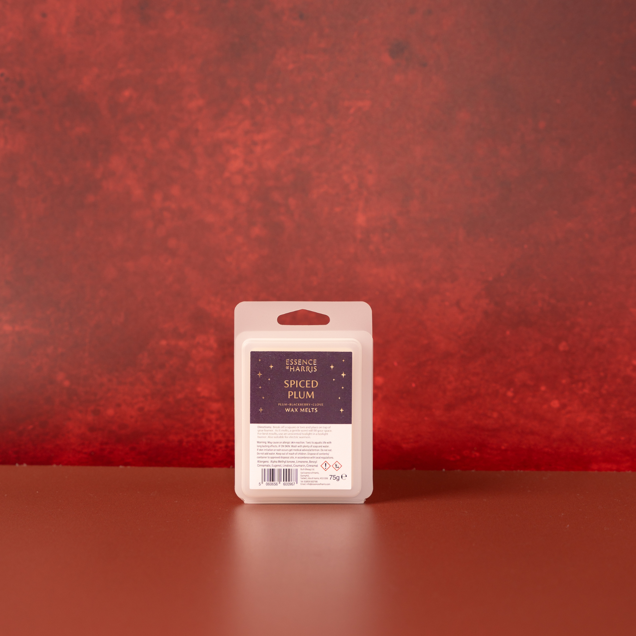 A single Spiced Plum wax melt bar stands upright on a reddish-brown surface against a textured red background.