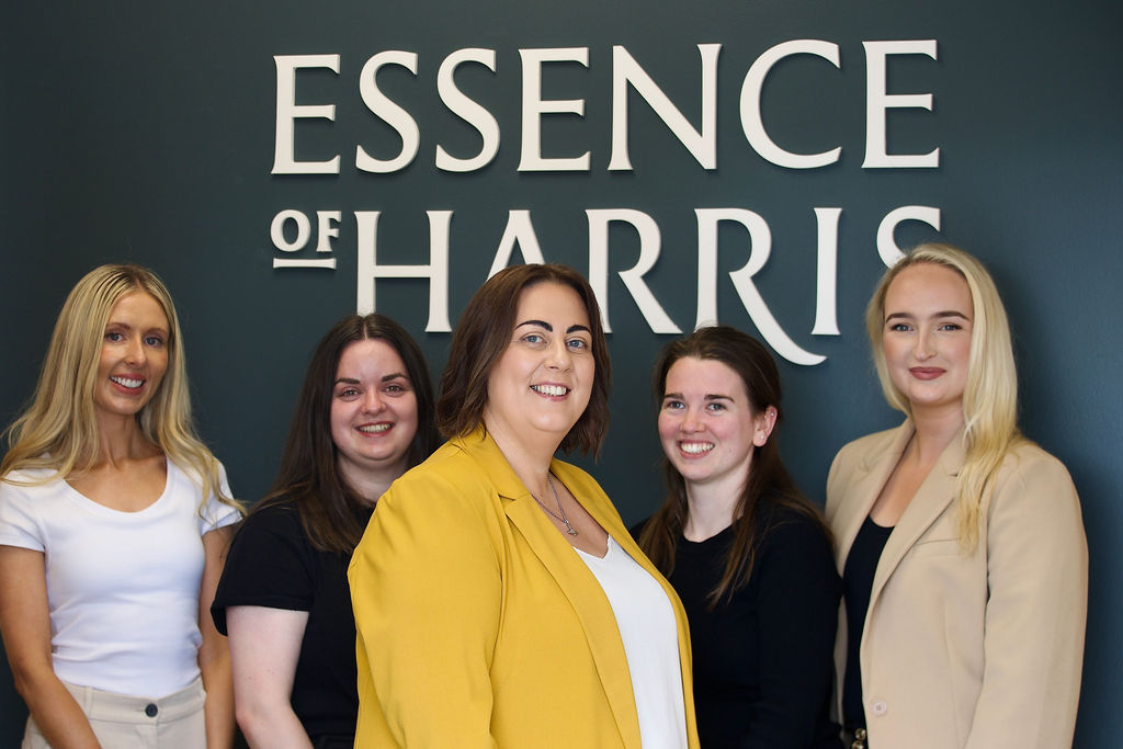 Five members of Essence of Harris all-female team standing together in a line, in-front of dark wall with logo