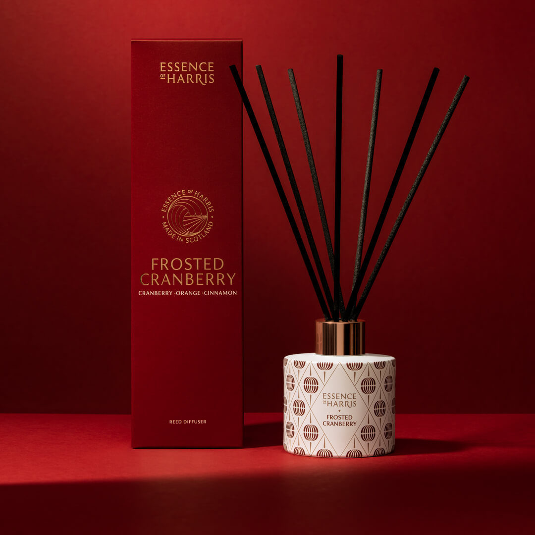 Frosted cranberry Christmas reed diffuser with festive pattern and black reeds next to red and gold box