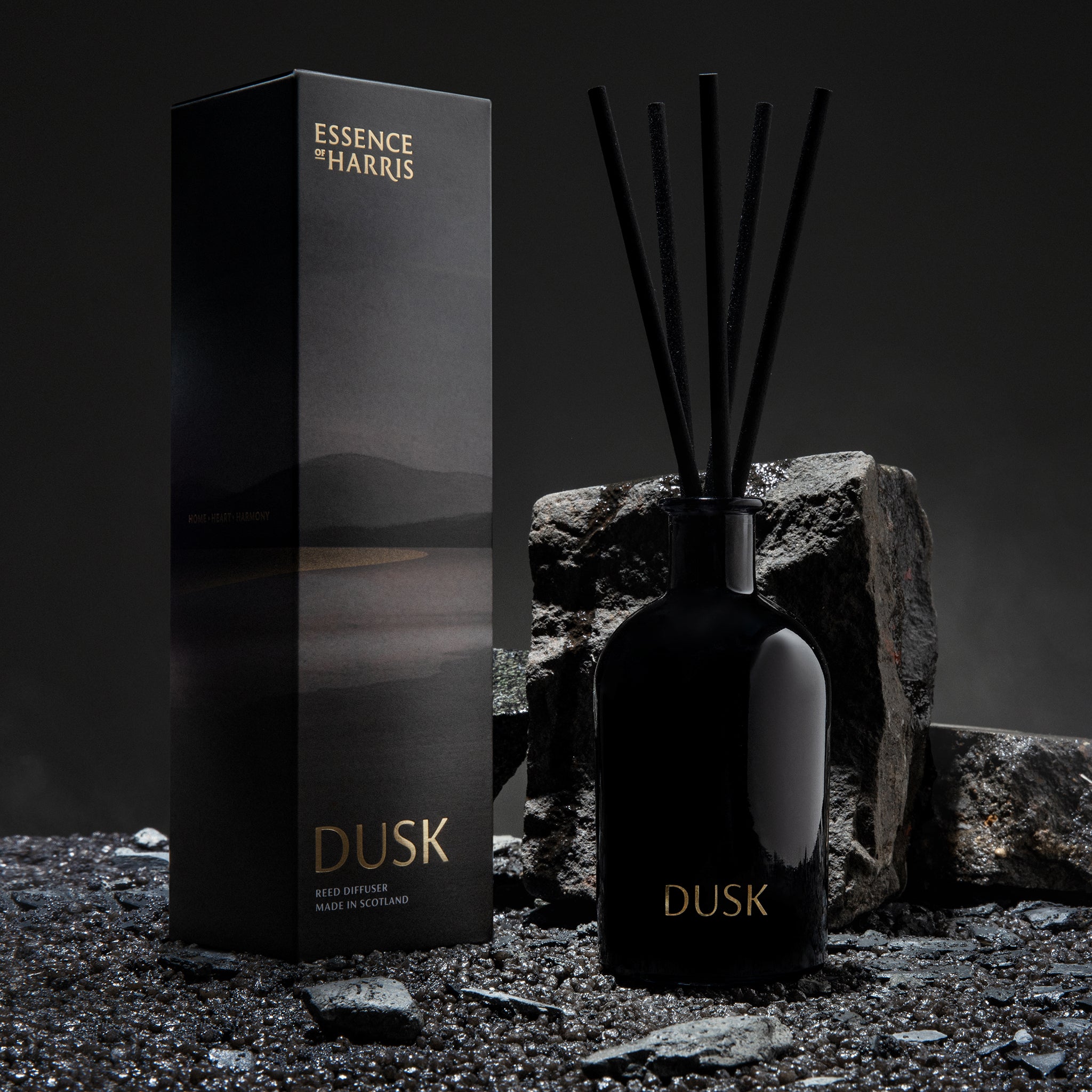Dusk, wild rhubarb reed diffuser in black smoked glass bottle with gold writing next to sunset illustrated box