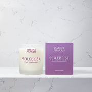 Essence of Harris Seilebost black pomegranate and plum soy wax candle in frosted glass vessel next to purple branded candle box