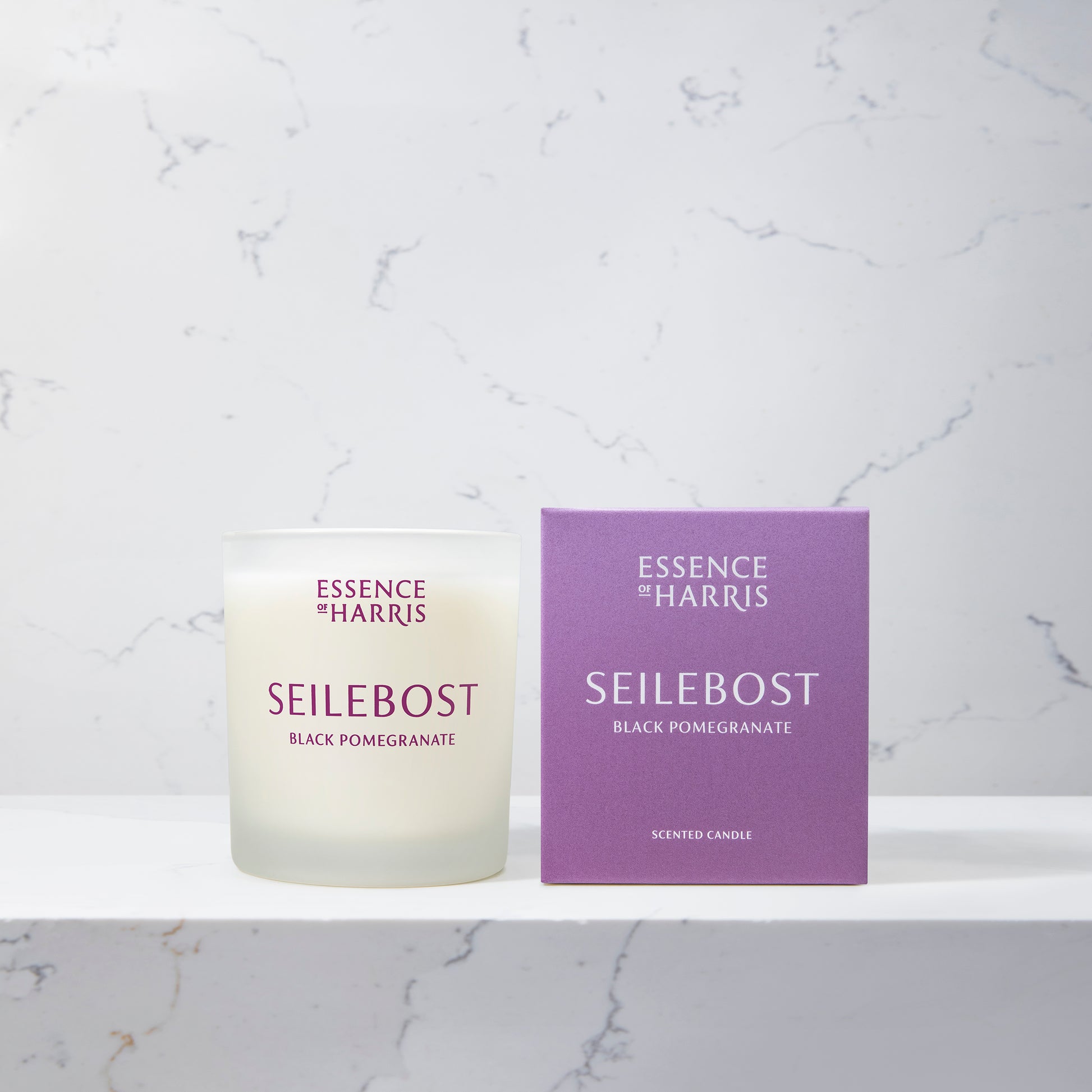Essence of Harris Seilebost black pomegranate and plum soy wax candle in frosted glass vessel next to purple branded candle box